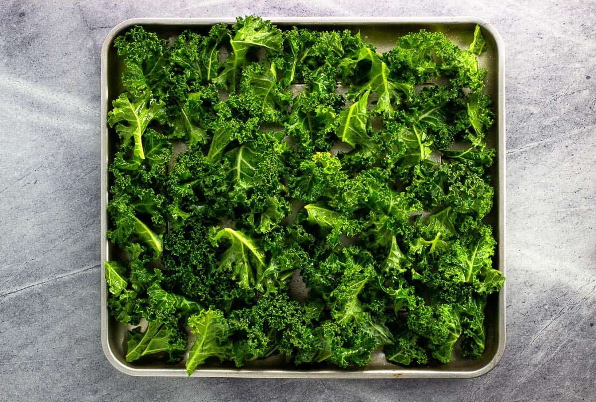 Oil rubbed kale leaves arranged on an air fryer tray.
