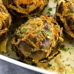 A close-up of a stuffed artichoke in a pan of cooking liquid.