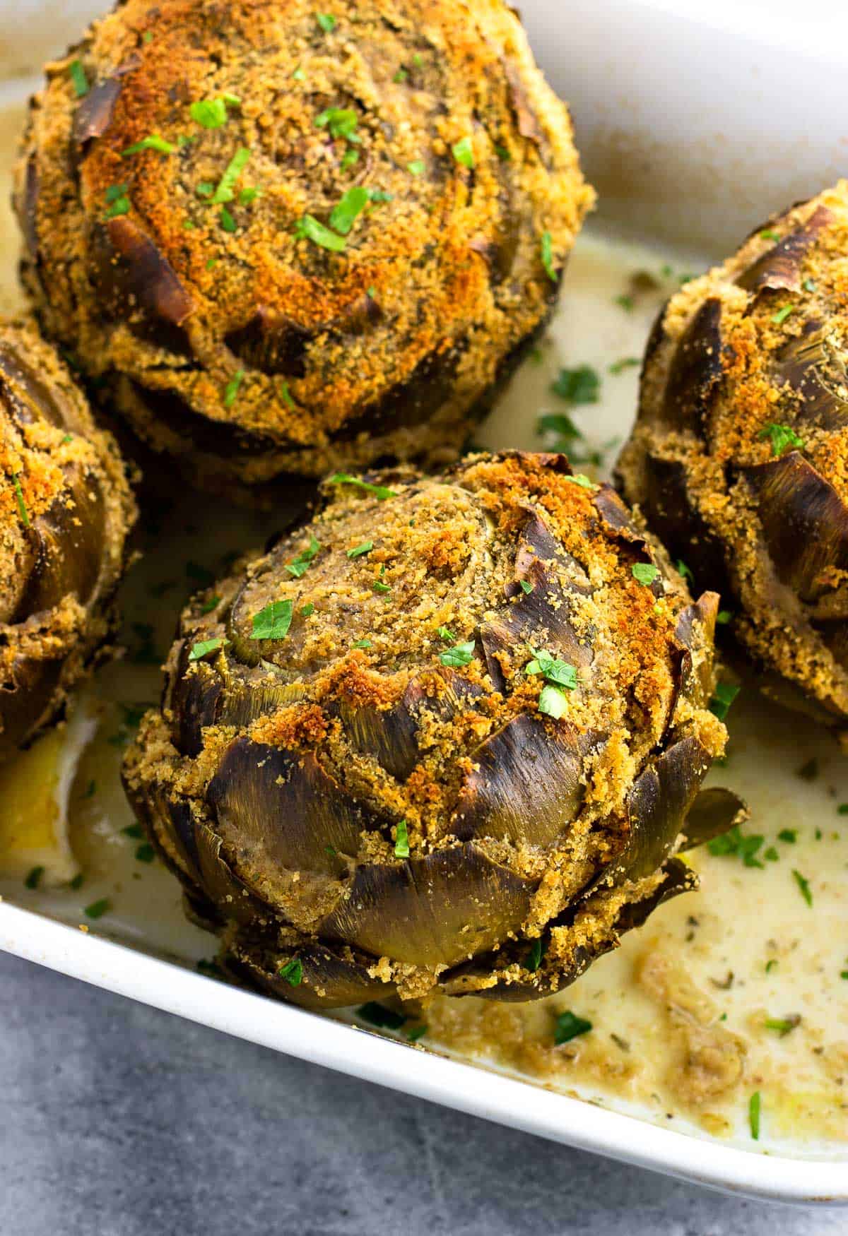 A pan of four stuffed artichokes after being cooked.