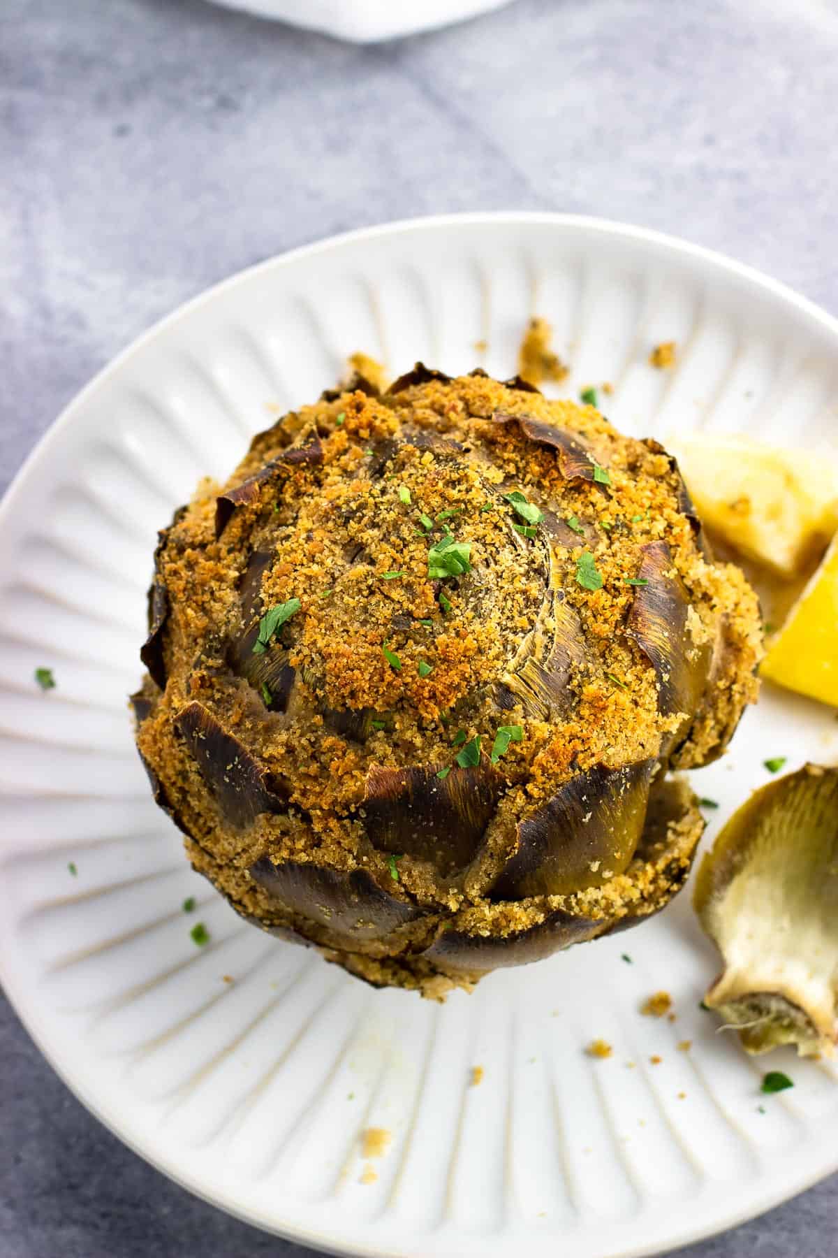 A stuffed artichoke on a plate with lemon wedges.