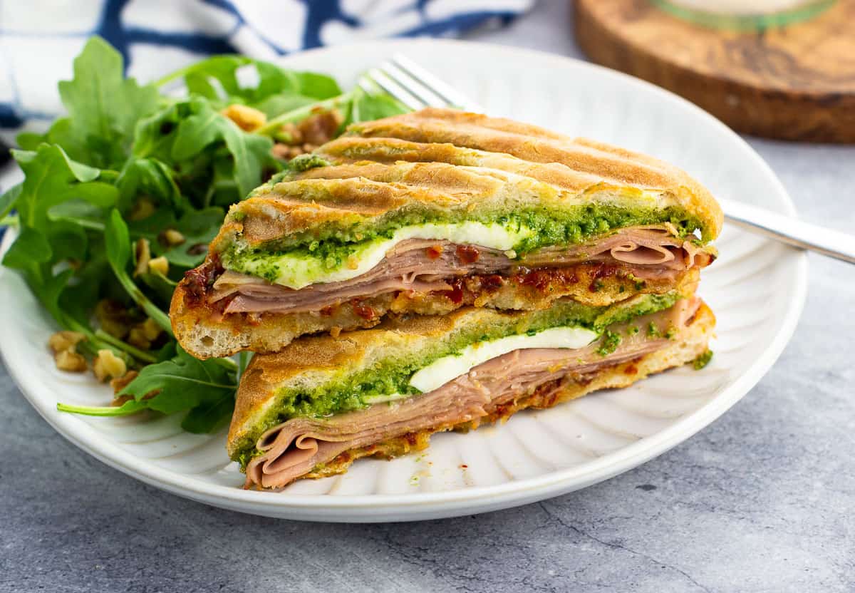 Two halves of a mortadella panini stacked on top of each other on a plate with salad.