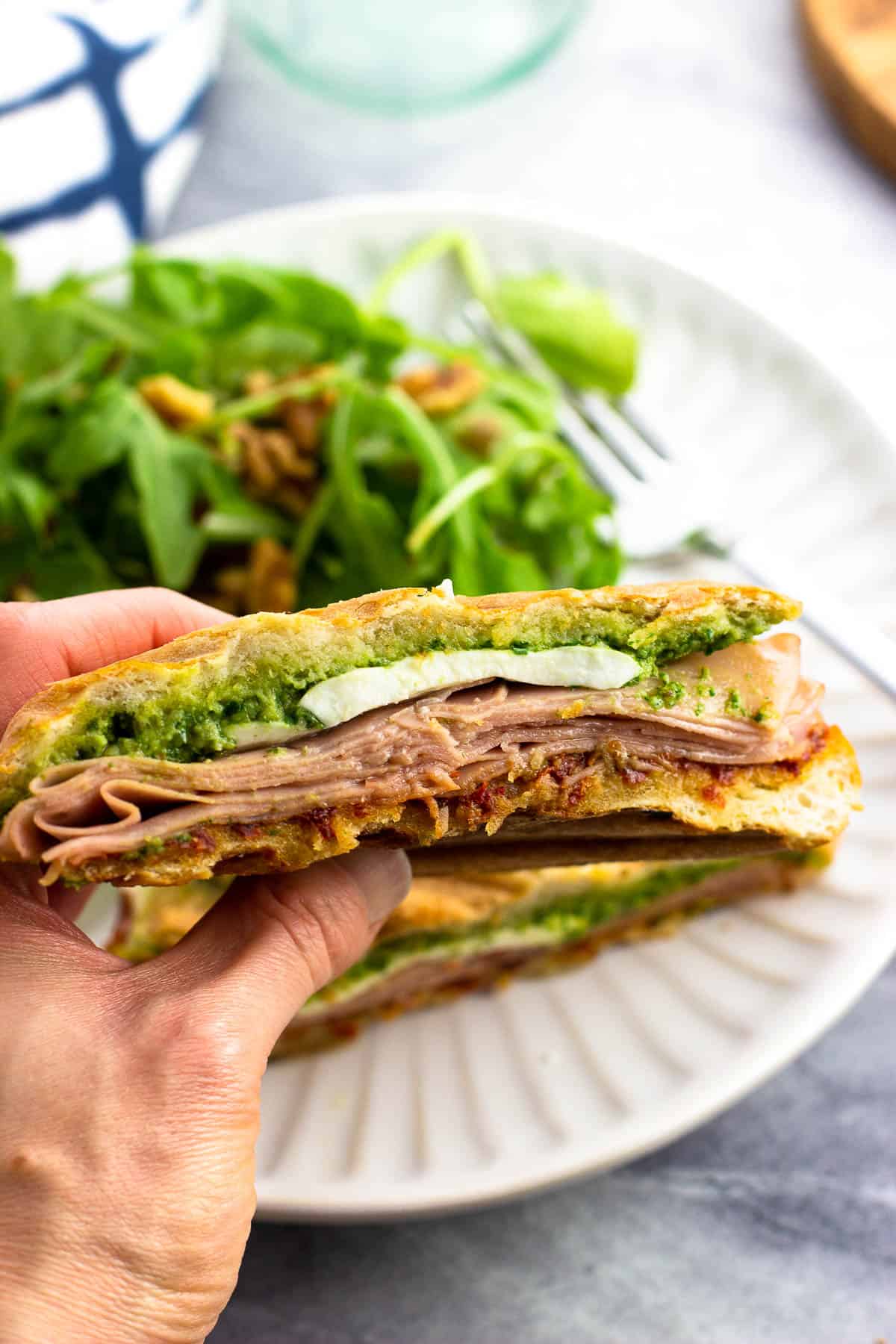 A hand holding up one side of a mortadella sandwich.