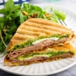 Two halves of a mortadella panini stacked on top of each other on a plate with salad.