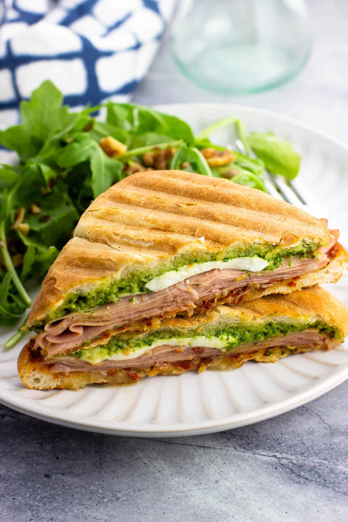 Two halves of a mortadella panini stacked on top of each other on a plate with salad.