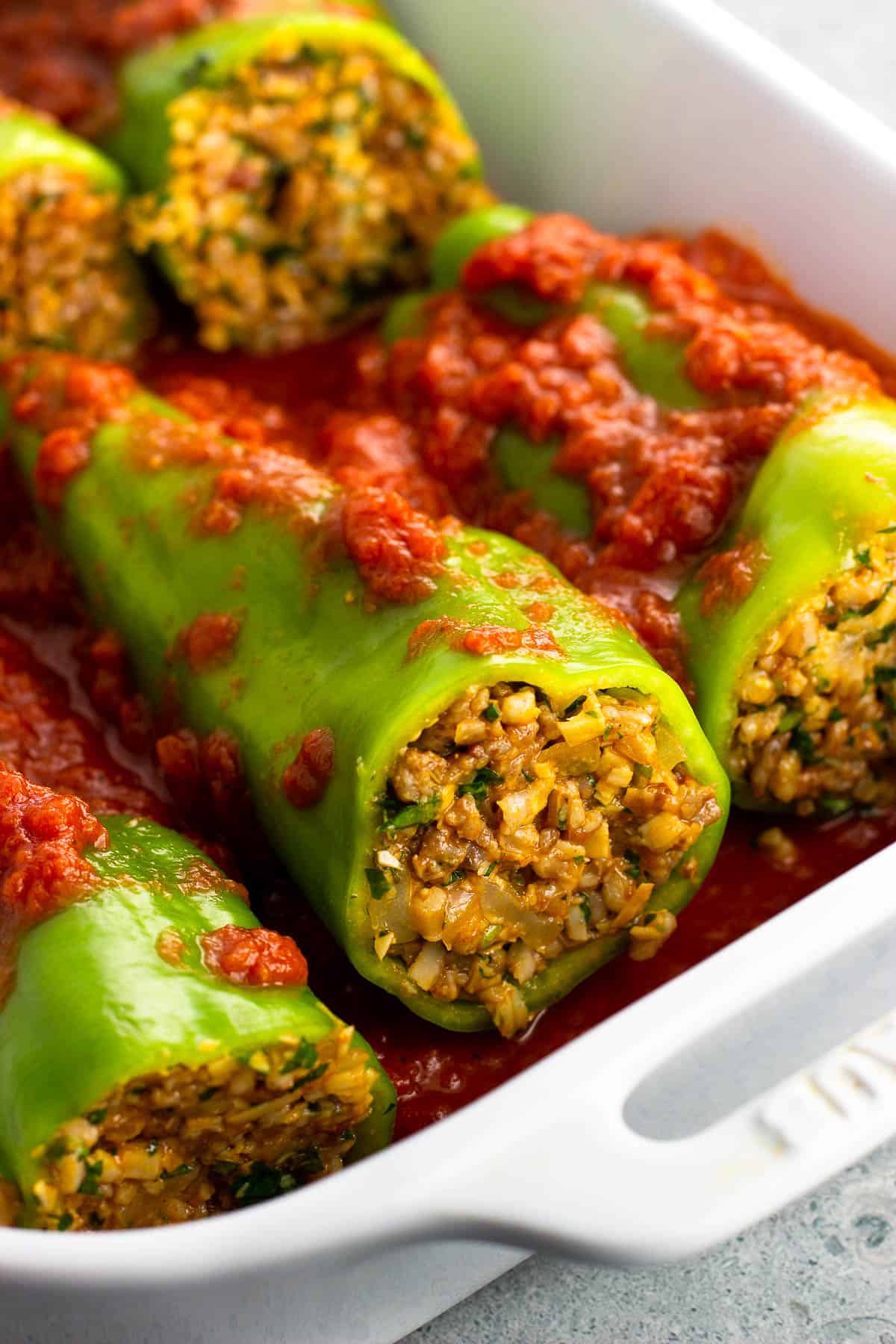 Cubanelle peppers stuffed with sausage and farro in a baking dish with marinara sauce.