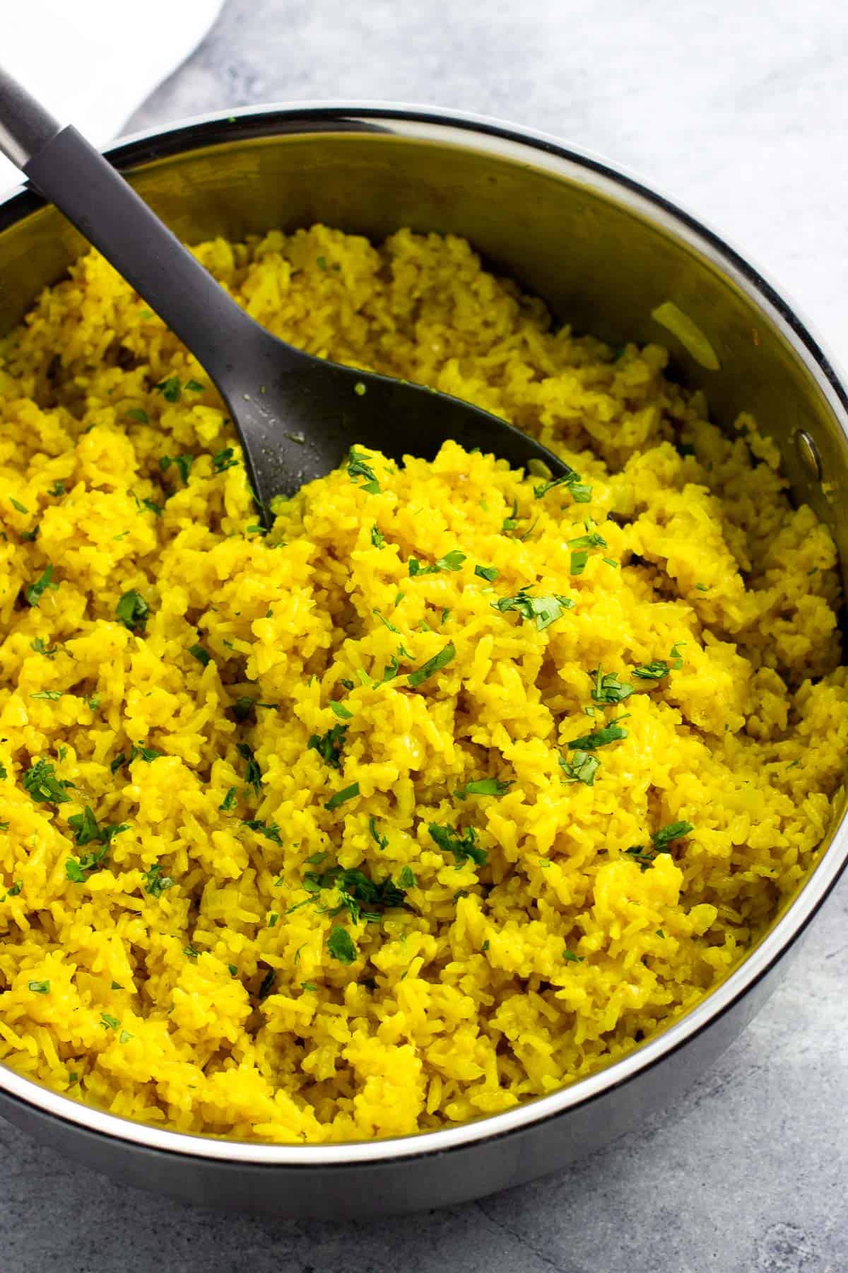Turmeric coconut rice in a pan with a serving spoon scooped in.