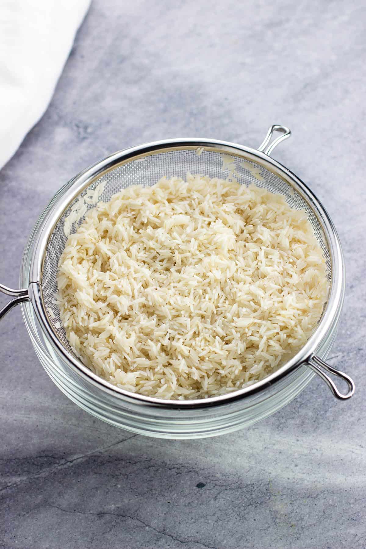 Basmati rice in a large mesh strainer after being rinsed.