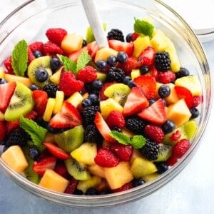 Fruit salad tossed in anise cinnamon syrup in a serving bowl garnished with mint leaves.