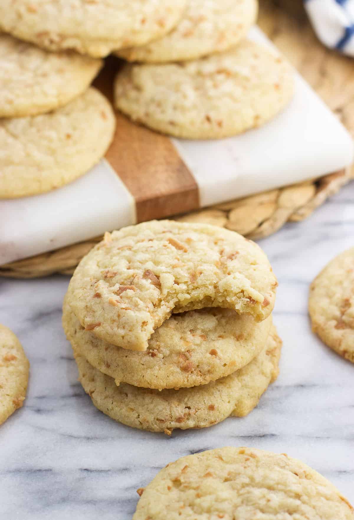 A stack of three coconut cookies on a marble board in front of more cookies.