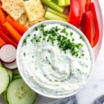 Cottage cheese dip decorated with chives on a platter with vegetables and crackers.