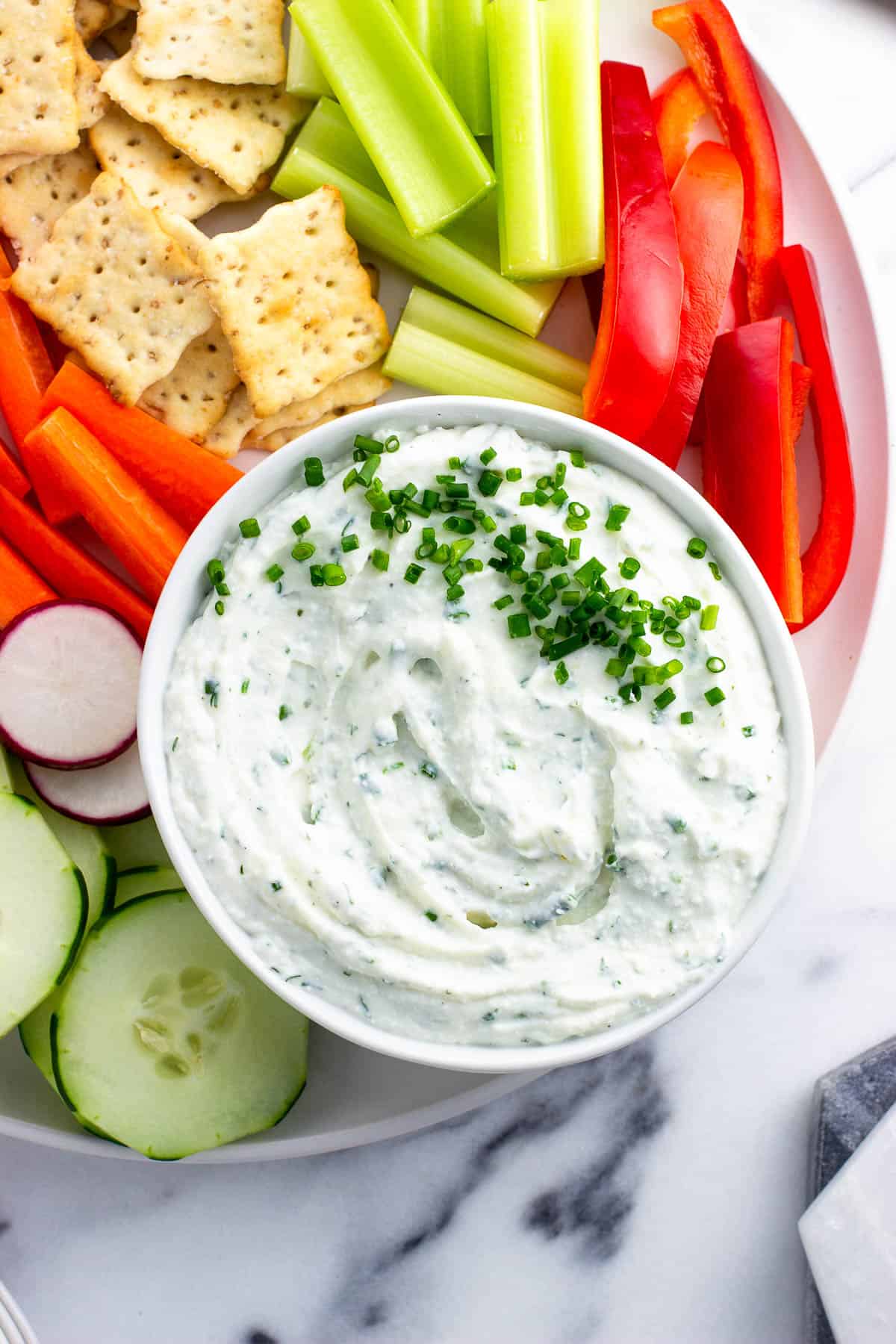 Cottage cheese dip decorated with chives on a platter with vegetables and crackers.