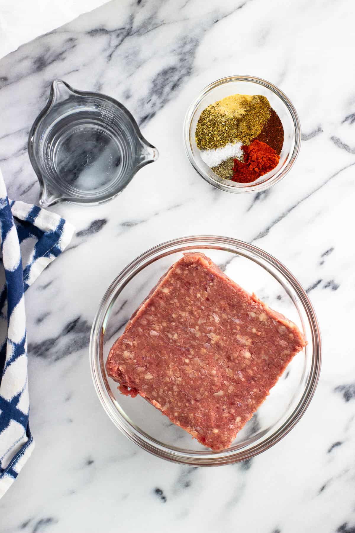 Water, raw ground beef, and taco seasoning in separate containers.