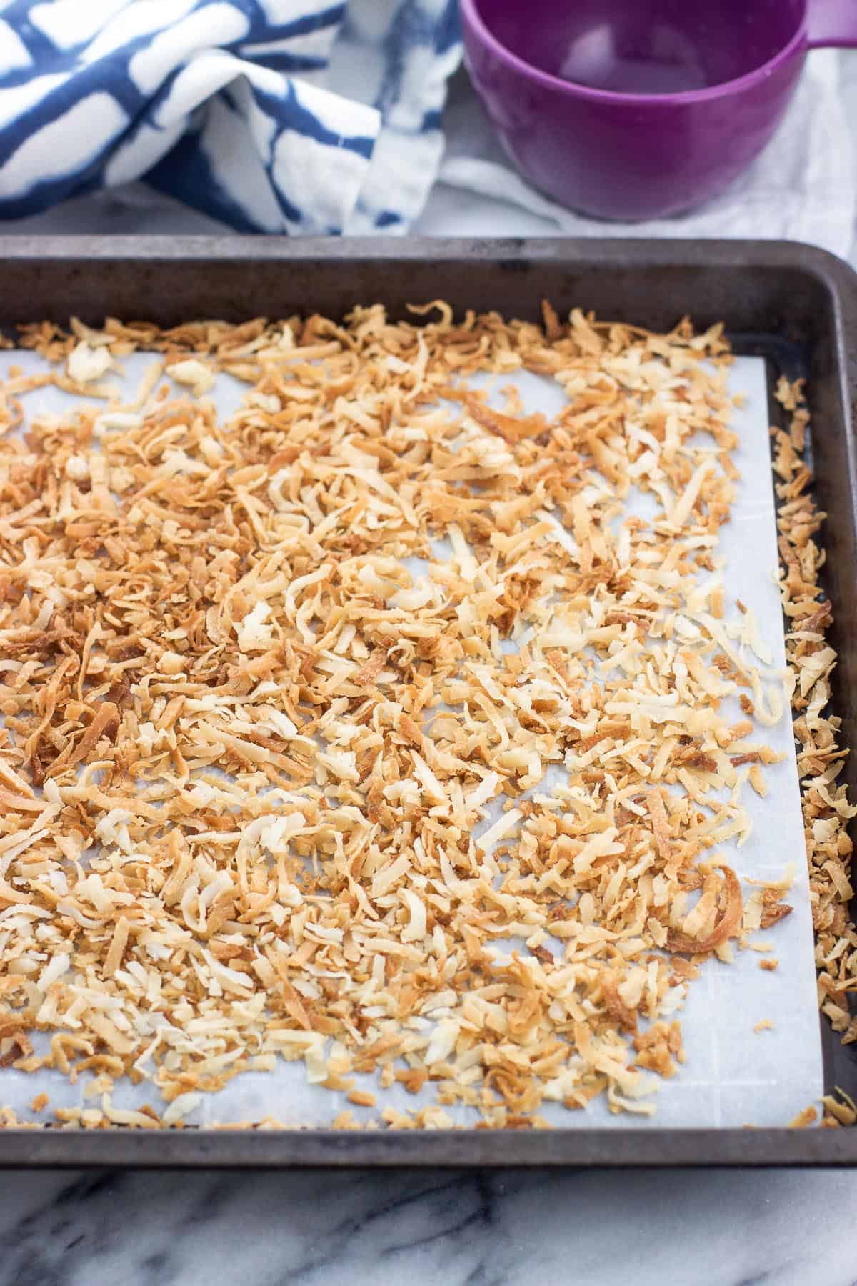 A parchment paper-lined sheet pan with toasted snowflake coconut on it.