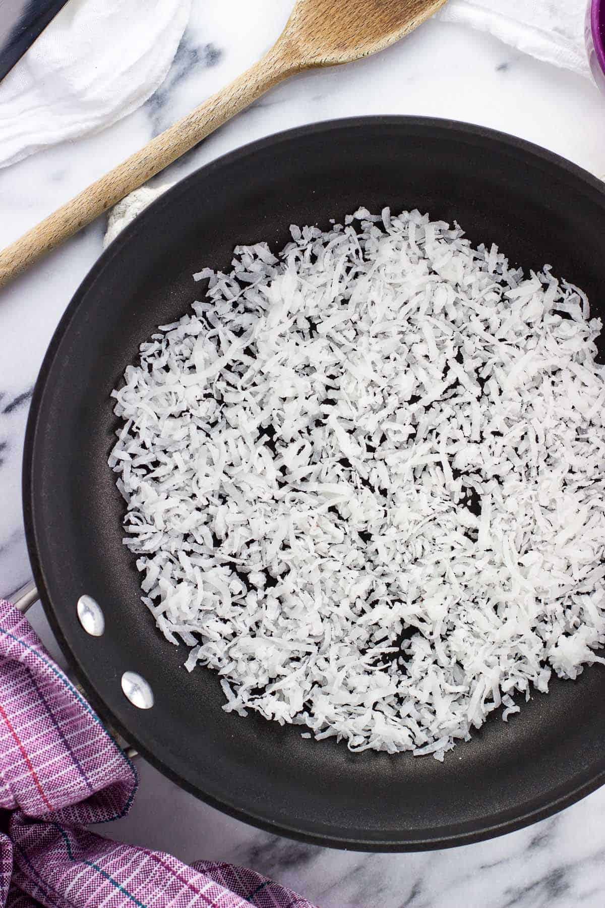 Sweetened flaked coconut in a pan before toasting.