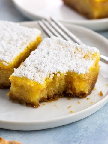 Two confectioners' sugar dusted lemon bars on a small plate with a forkful taken out of one.