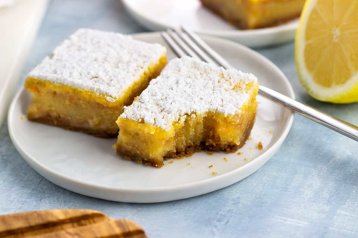 Two confectioners' sugar dusted lemon bars on a small plate with a forkful taken out of one.