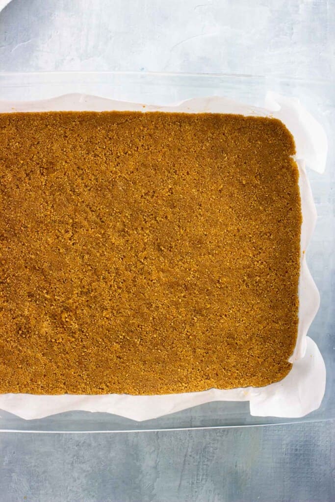 Baked graham cracker crust in a parchment-lined pan.