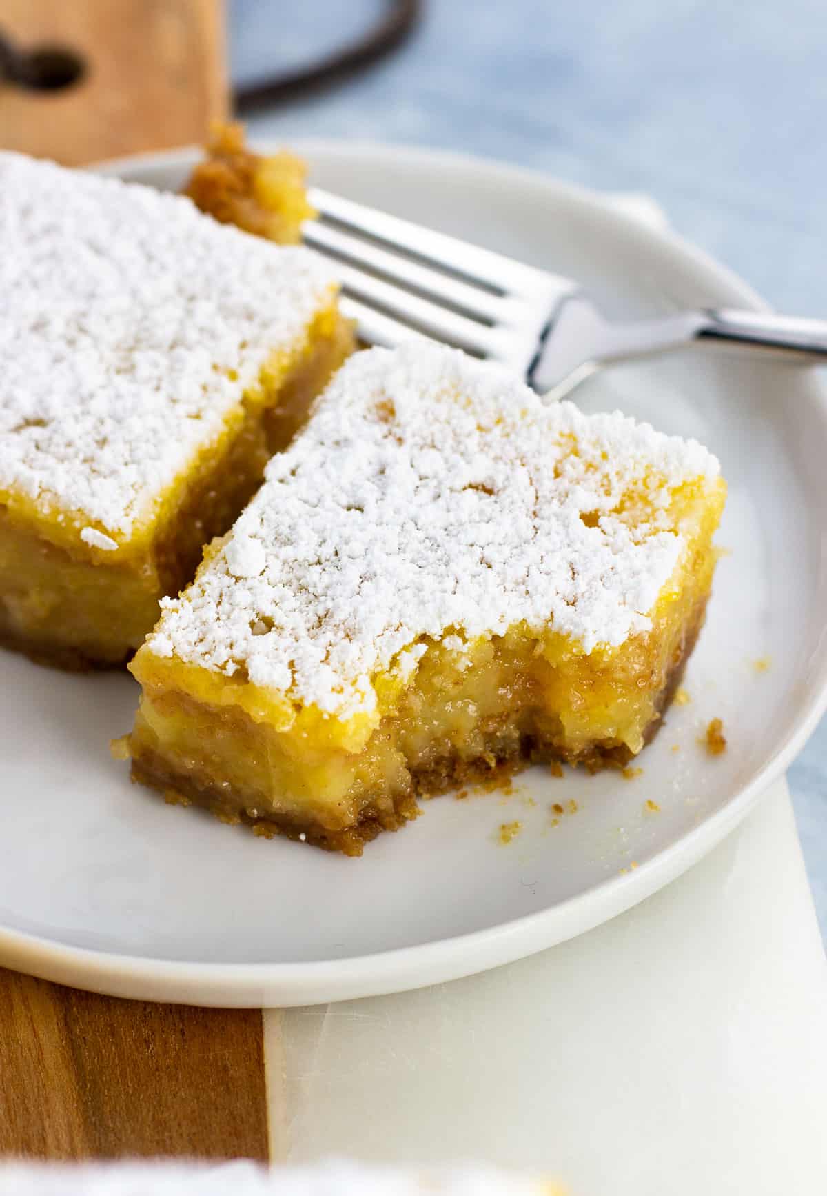 Two confectioners' sugar dusted lemon bars on a small plate with a forkful taken out of one.