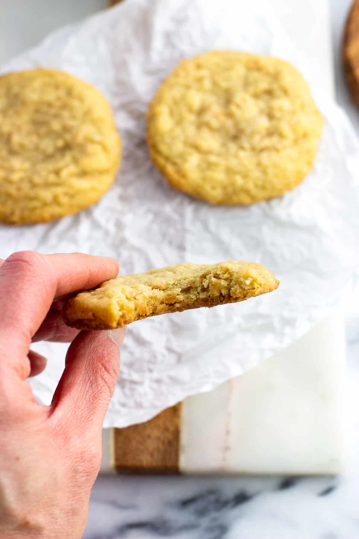 A hand holding up a cookie with a bite taken out of it.