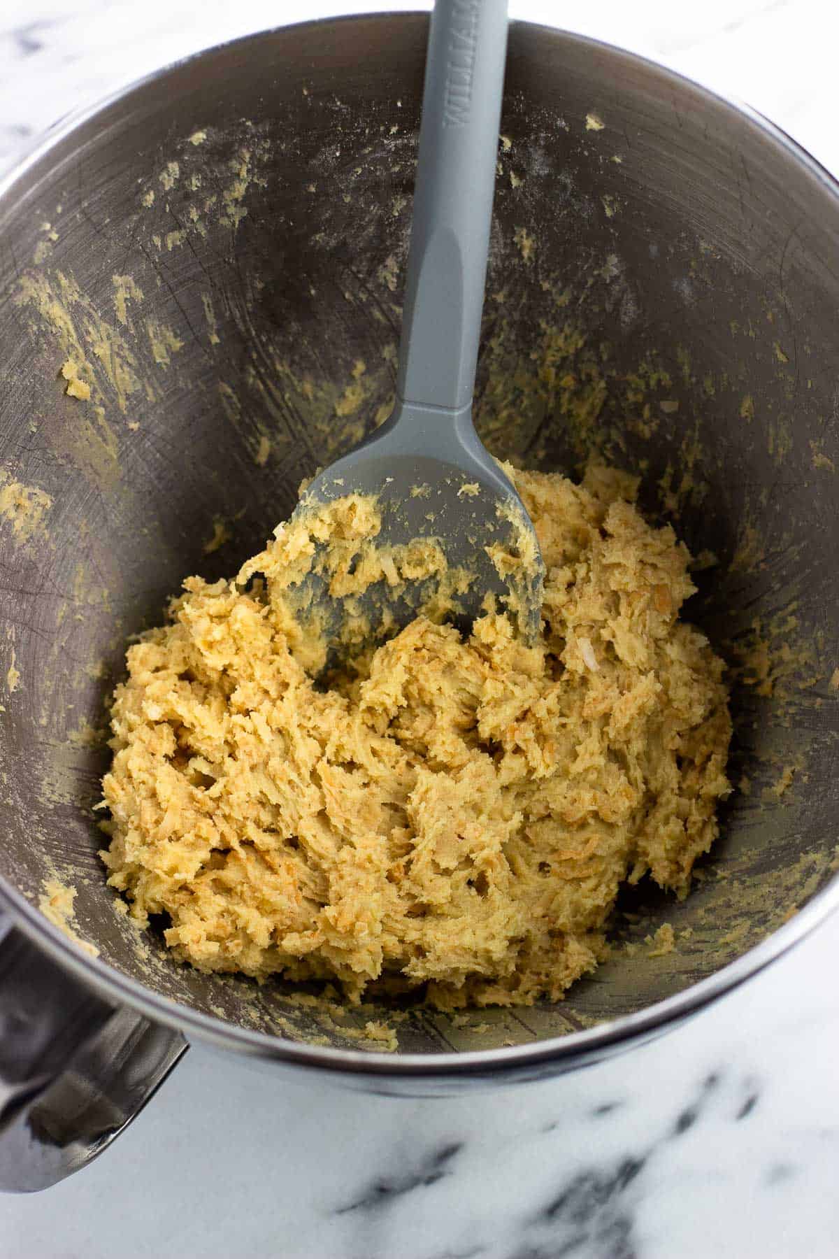 Toasted coconut flakes stirred into the cookie dough in a bowl.