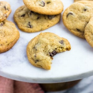 Cookies on a marble top cake stand with the front cookie having a big bite taken.