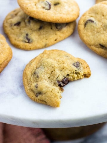 Cookies on a marble top cake stand with the front cookie having a big bite taken.