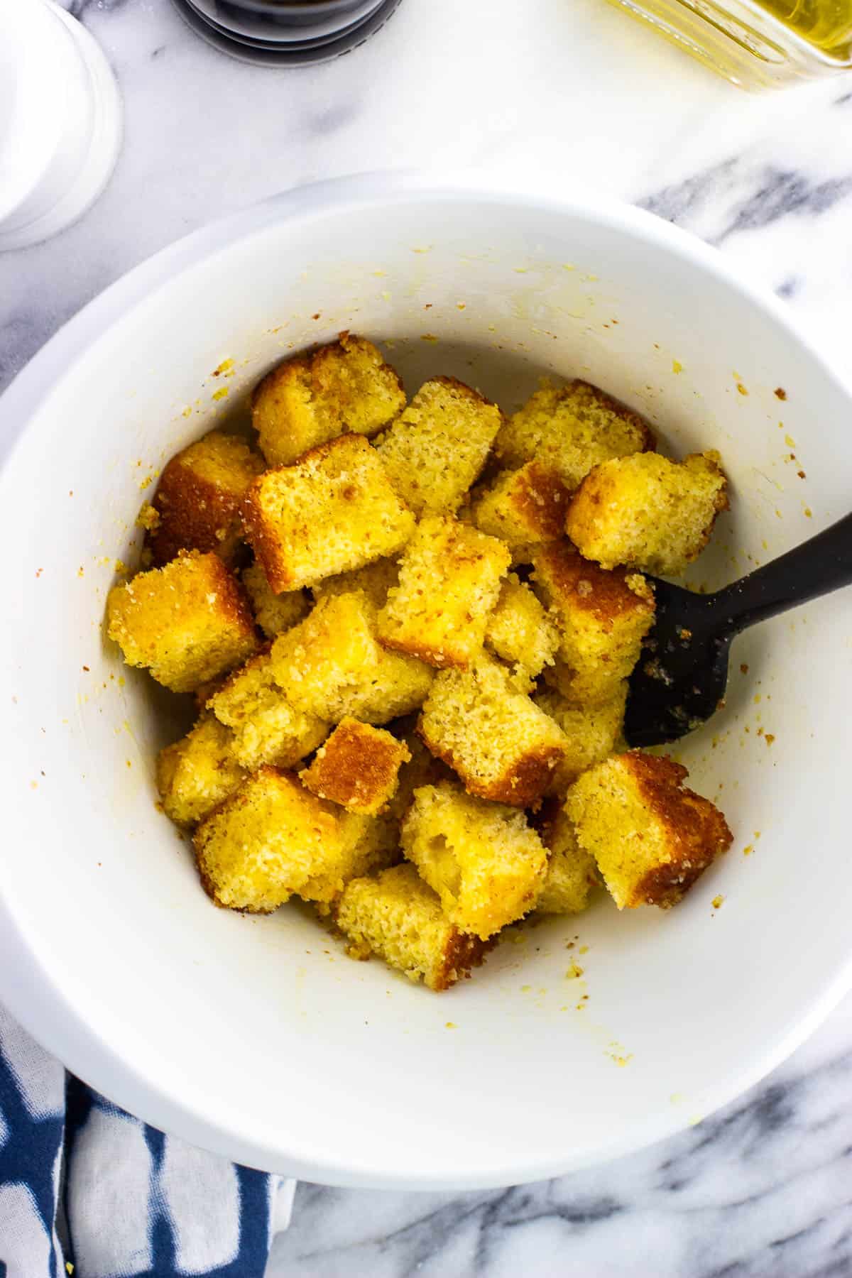 Stale cubed cornbread in a mixing bowl tossed in olive oil.