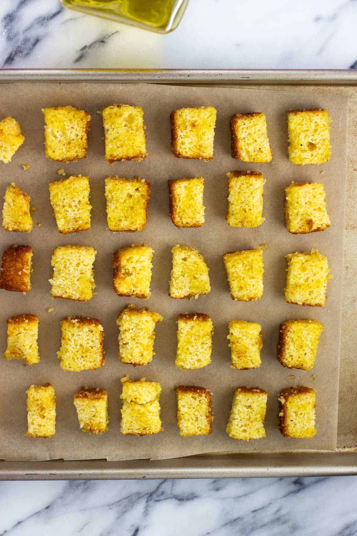 Oil-coated cornbread cubes on a baking sheet.