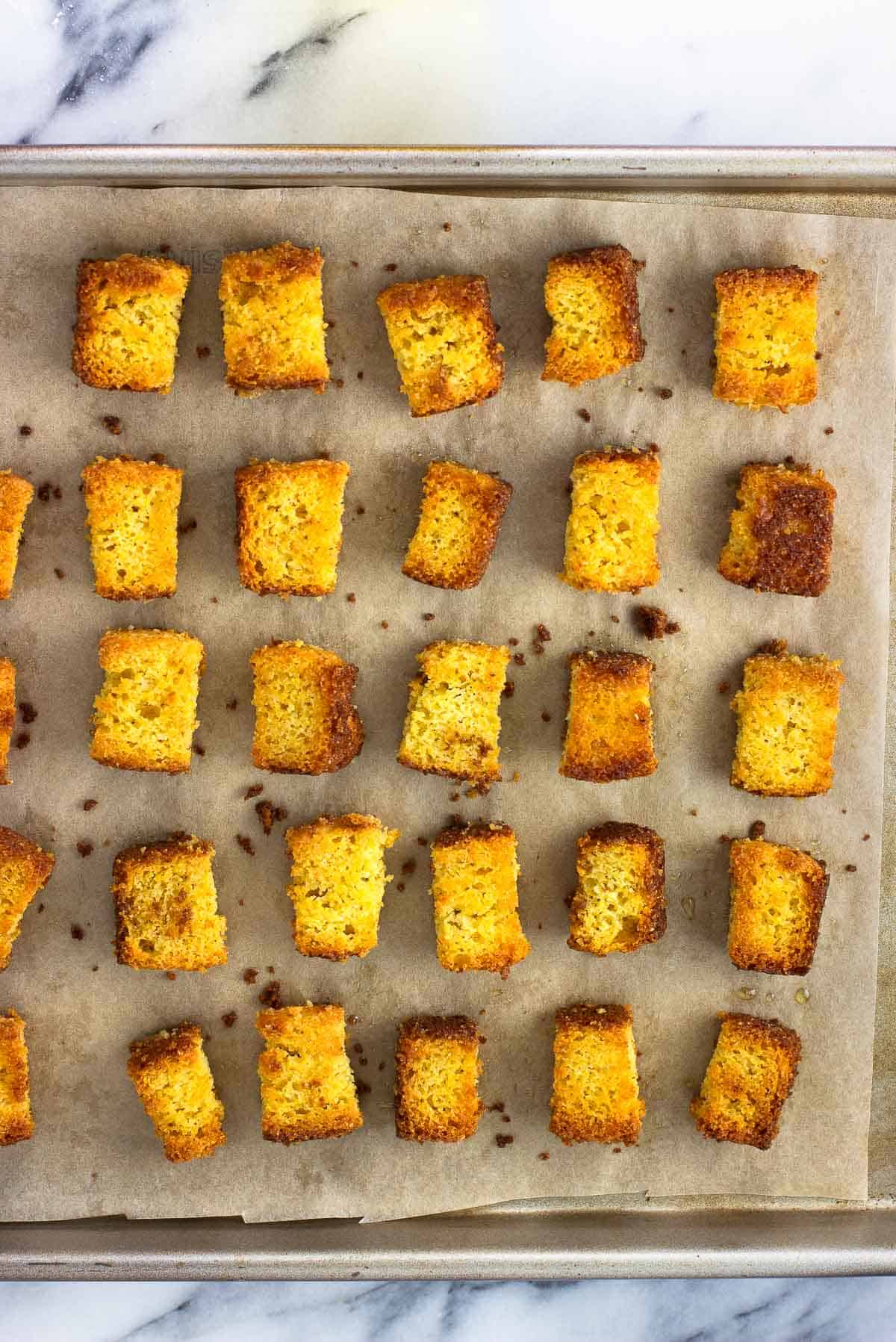 Cubed cornbread croutons on a parchment-lined pan.