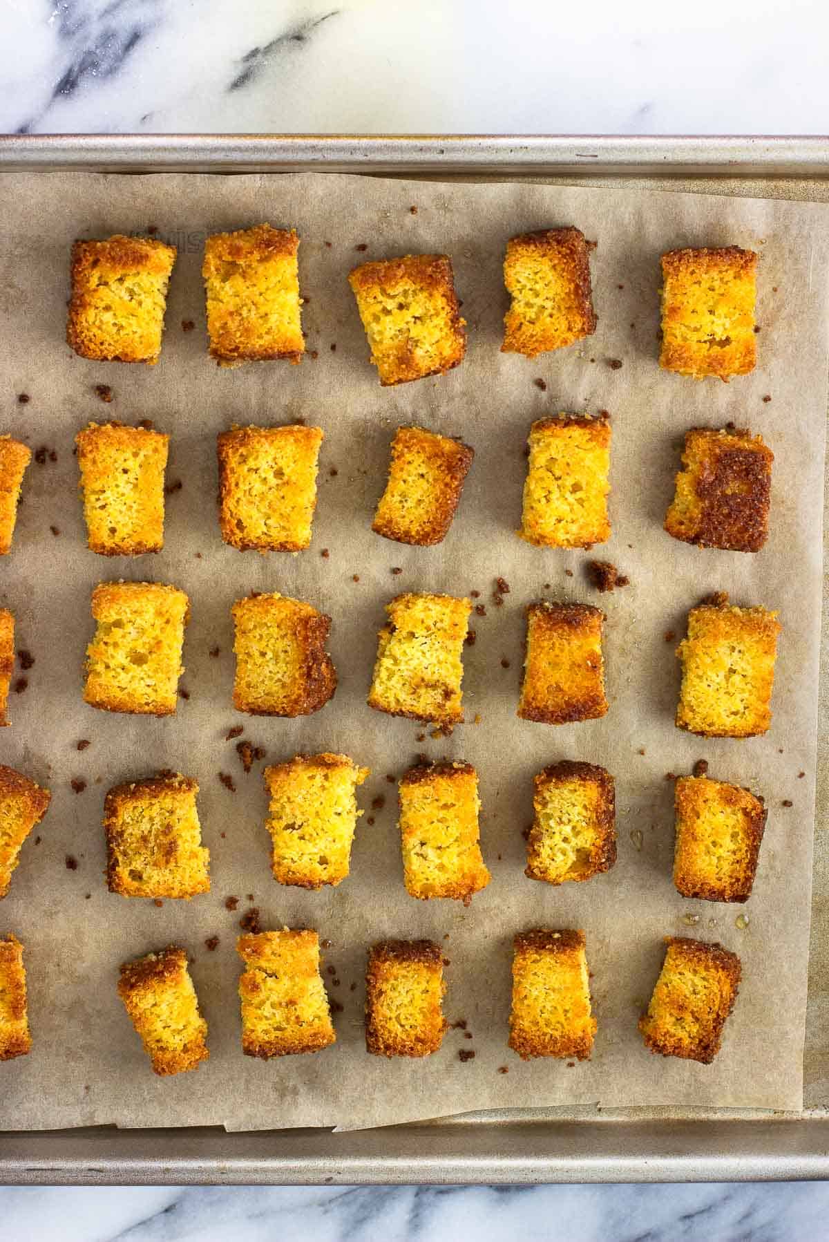 Cubed cornbread croutons on a parchment-lined pan.