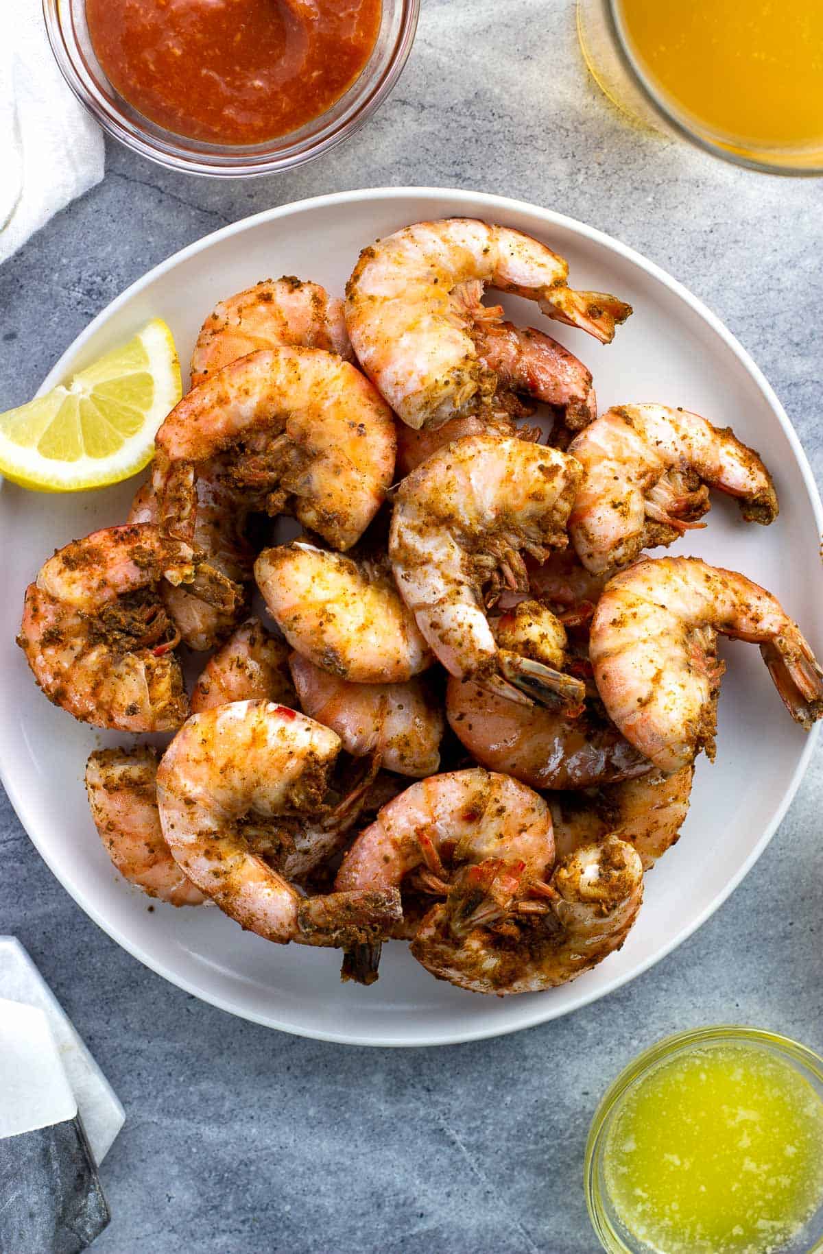 Old Bay steamed shrimp on a plate surrounded by cocktail sauce, melted butter, lemon wedge, and beer.