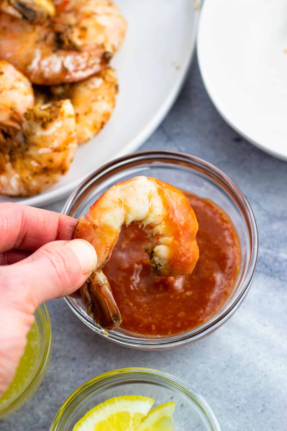 A peeled shrimp being dipped into a small bowl of cocktail sauce.