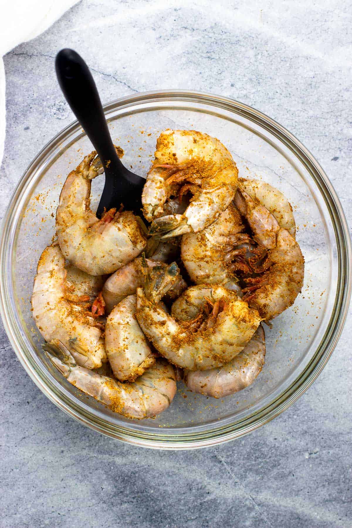 Raw shrimp tossed with Old Bay in a mixing bowl.