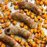 Roasted bratwurst, sweet potatoes, and onions on a sheet pan.
