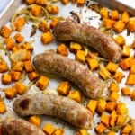 Cooked bratwurst, sweet potatoes, and onions on a sheet pan.