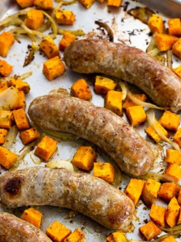 Cooked bratwurst, sweet potatoes, and onions on a sheet pan.
