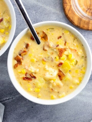 Two bowls of shrimp and corn chowder next to a bowl of salad and a glass of water.