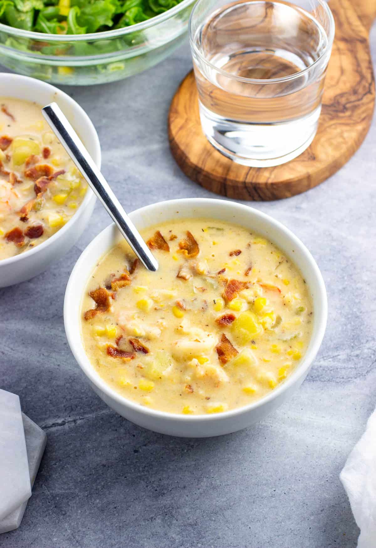 Two bowls of shrimp and corn chowder next to a bowl of salad and a glass of water.