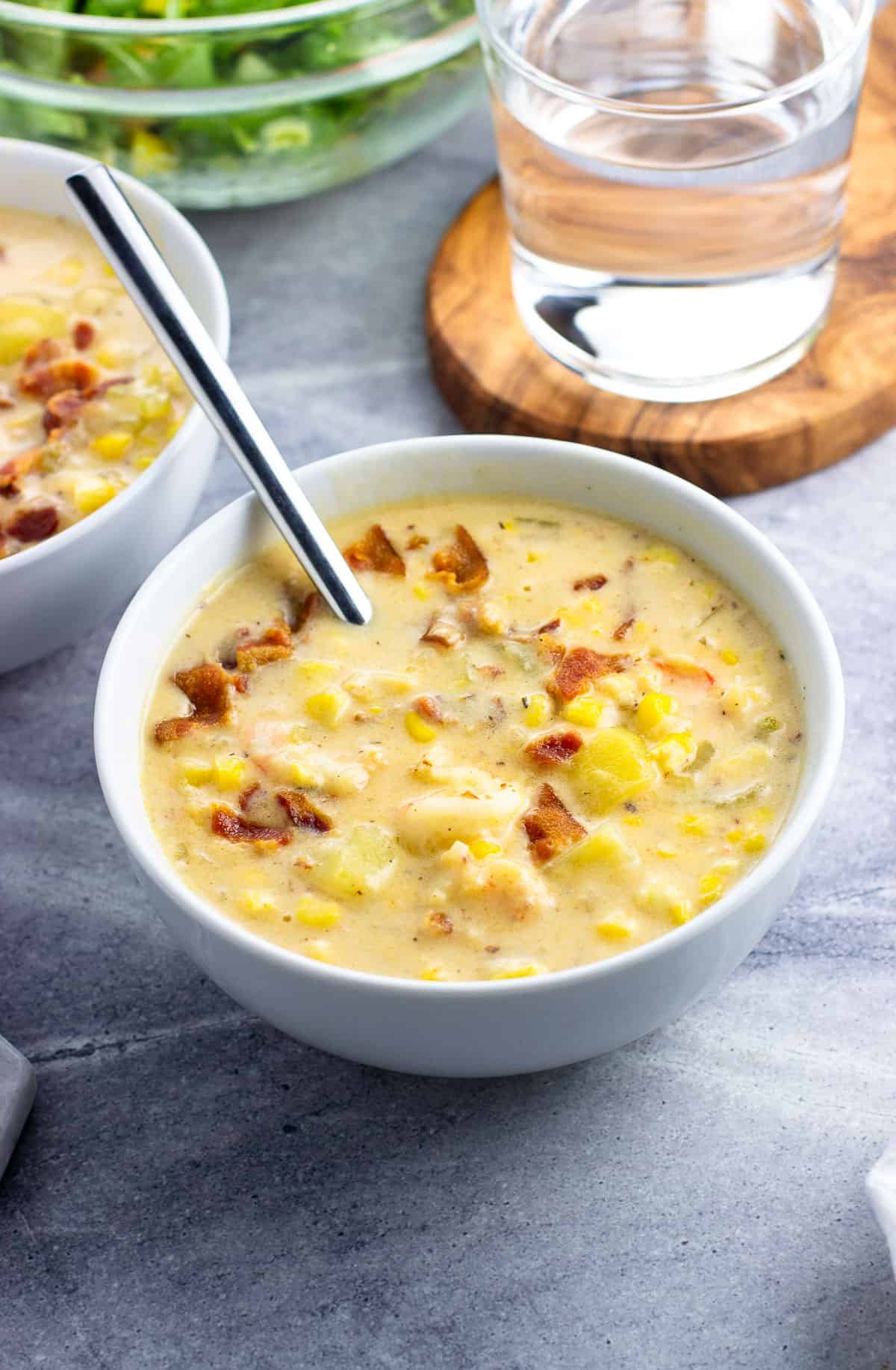 A bowl of corn and shrimp chowder topped with crumbled bacon.