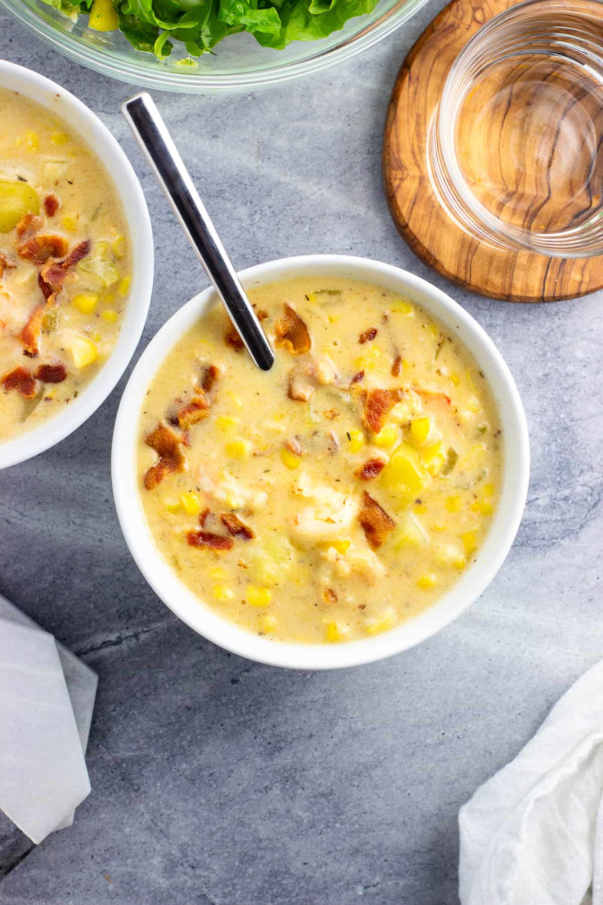 Two bowls of shrimp and corn chowder next to a bowl of salad and a glass of water.