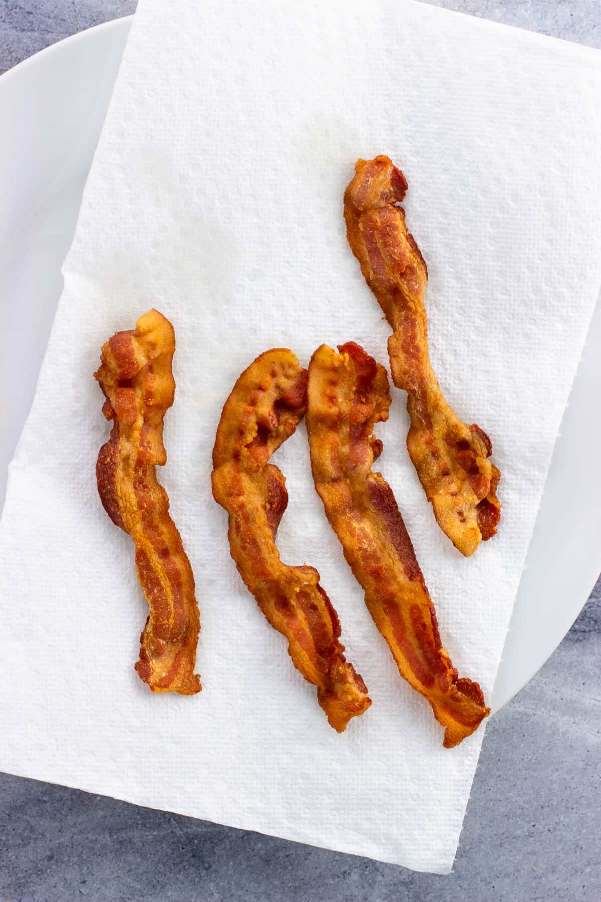 Four slices of cooked bacon on a paper towel-lined plate.