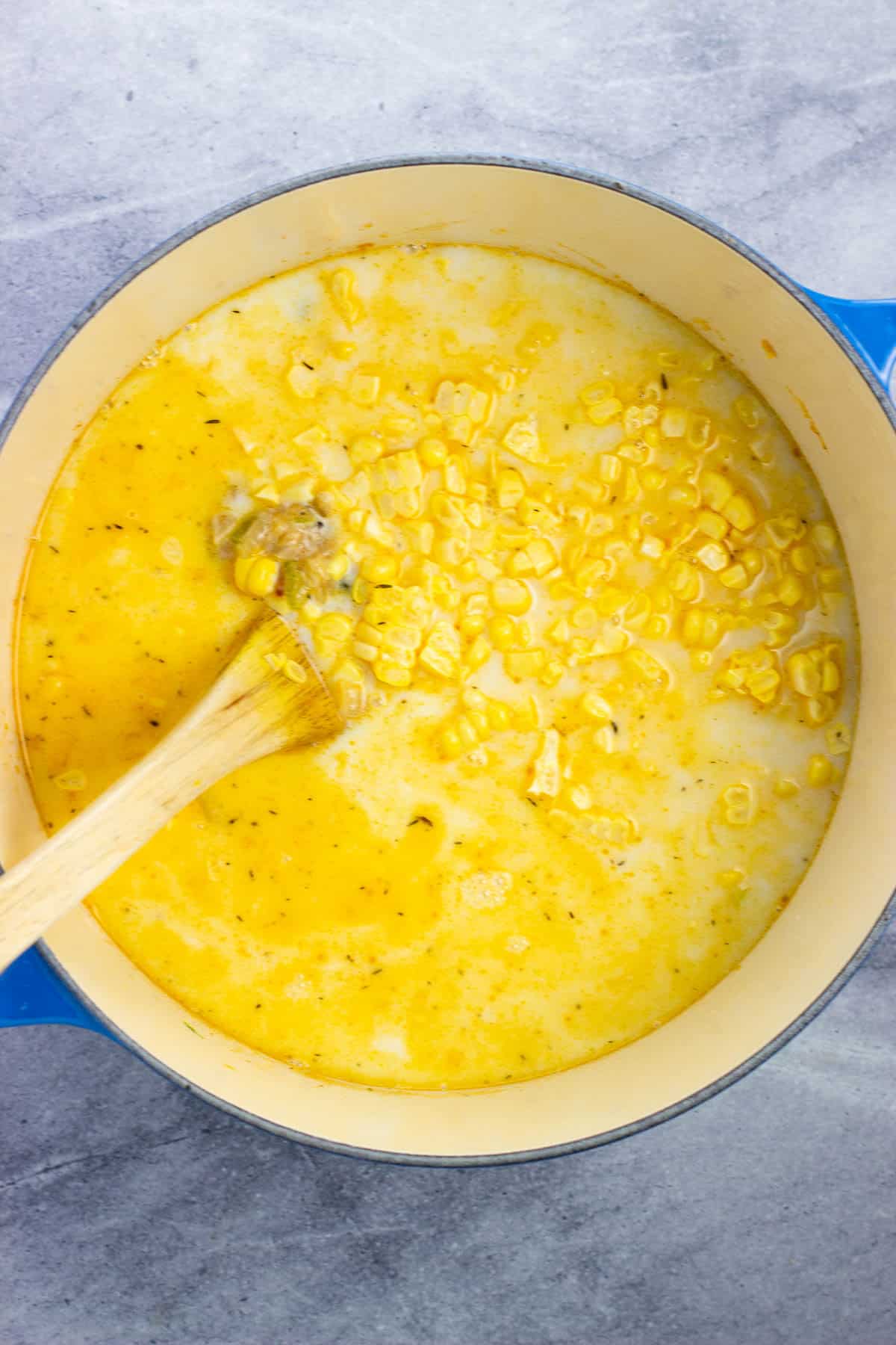 Soup liquid, potatoes, and corn kernels being stirred into the pot of chowder.