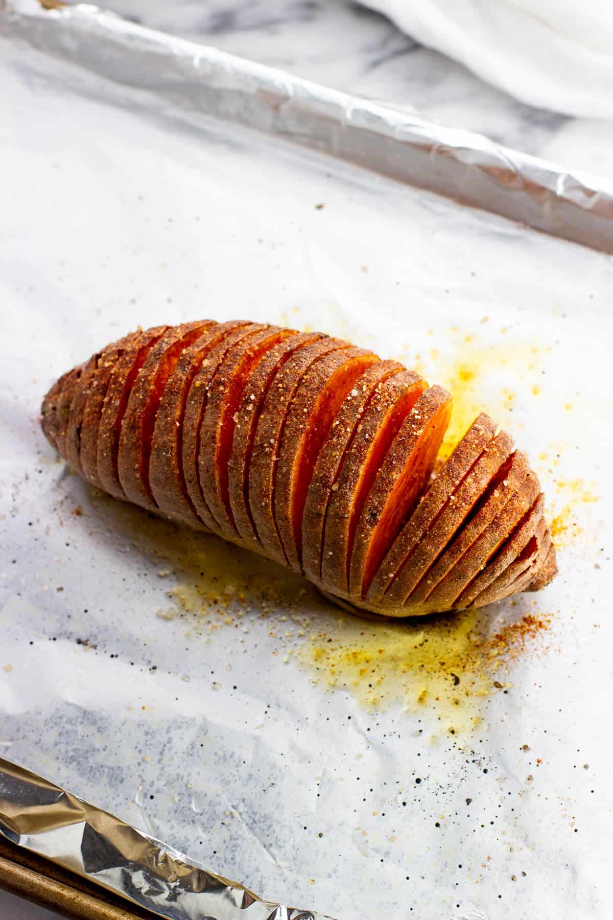 A hasselback sweet potato roasted on a foil-lined baking sheet.