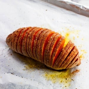 A hasselback sweet potato roasted on a foil-lined baking sheet.