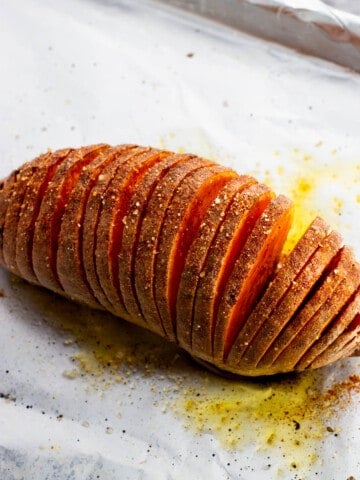 A hasselback sweet potato roasted on a foil-lined baking sheet.