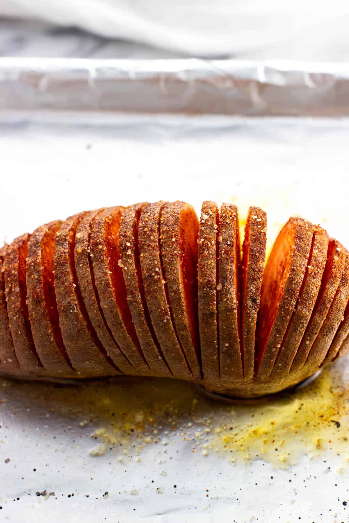 A roasted sweet potato cut hasselback-style on a baking sheet.