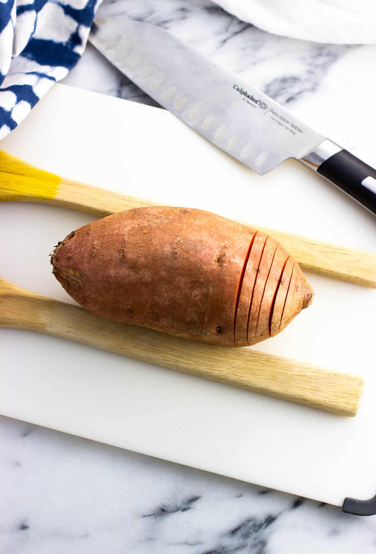 Beginning to make thin slices in a sweet potato on a cutting board.