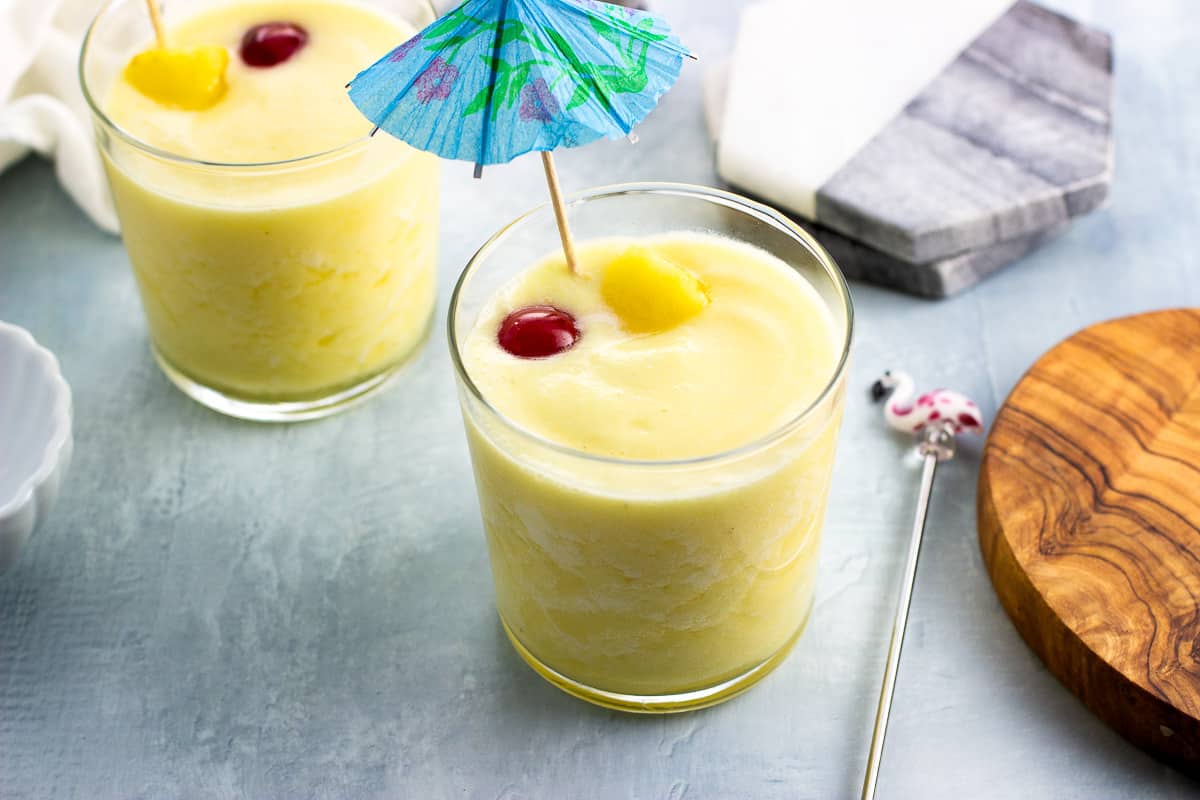 Two piña coladas garnished with pineapple, maraschino cherries, and a paper drink umbrella.