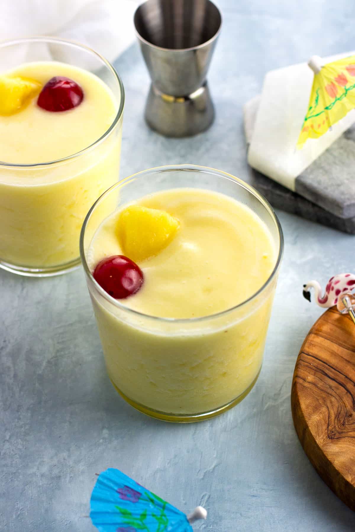 Two less-sugar piña coladas garnished with a pineapple chunk and maraschino cherry.