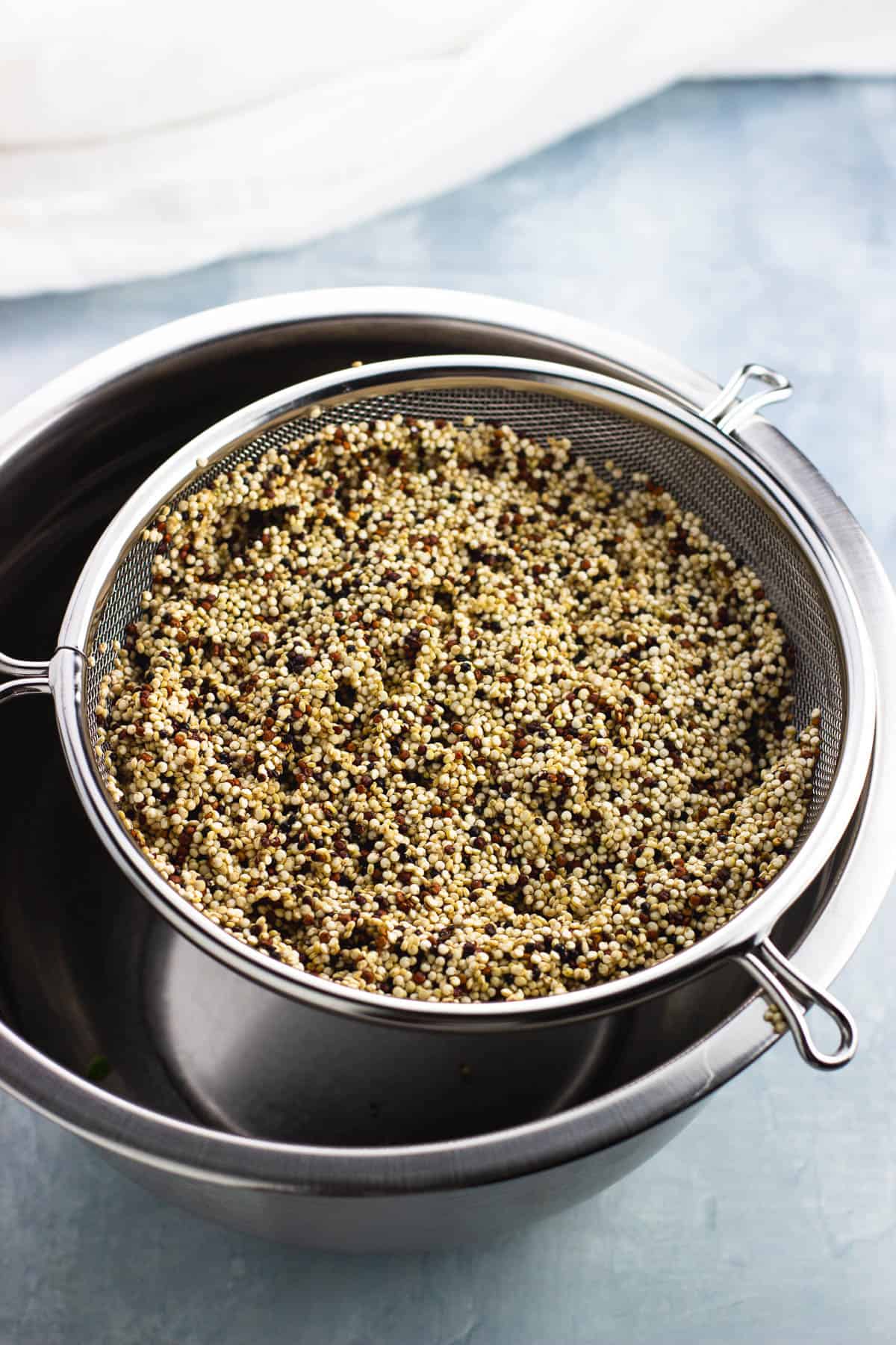Rinsed quinoa in a large metal sieve set over a bowl.